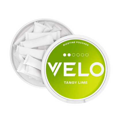 Un envase redondo y abierto de color blanco de VELO Tangy Lime revela varias bolsitas blancas en su interior. La tapa presenta un degradado verde con texto en negrita, que resalta el sabor a lima ácida y la nicotina afrutada de cada bolsa.