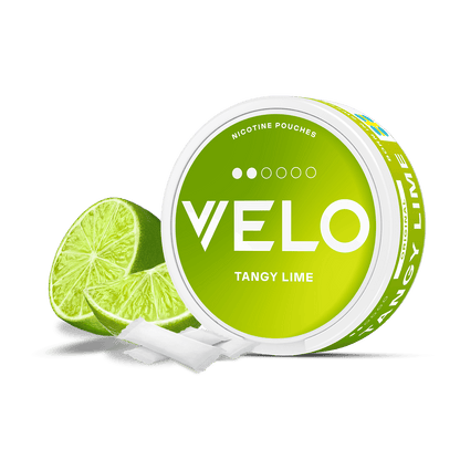 Un envase de bolsitas de nicotina VELO Tangy Lime verde lima descansa junto a una lima en rodajas y dos bolsitas blancas, todo sobre un fondo blanco, resaltando la nicotina afrutada y el sabor a lima ácida. Unas letras blancas decoran el envase.